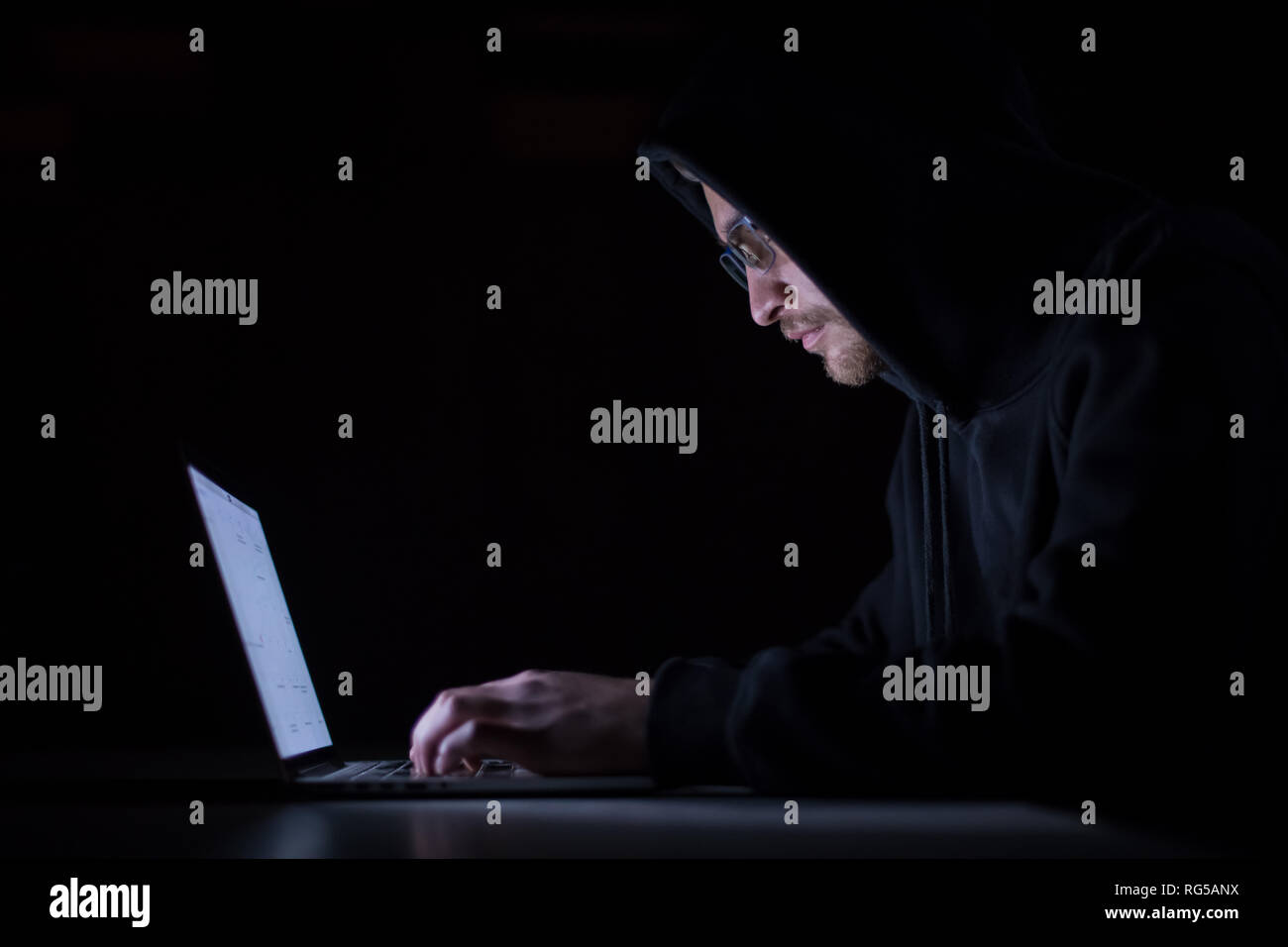 Young talented hacker using laptop computer while working in dark ...