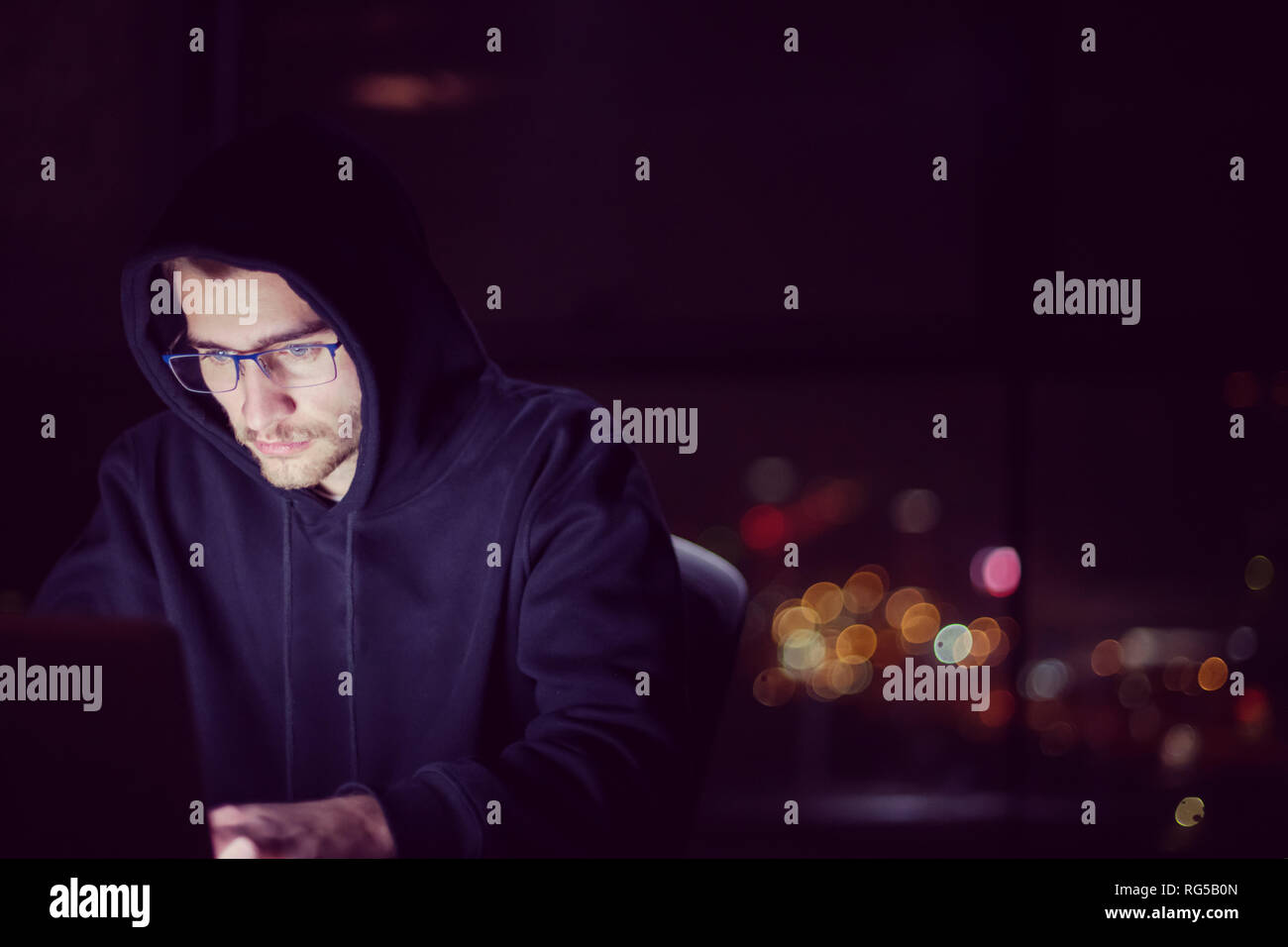 Young talented hacker using laptop computer while working in dark ...
