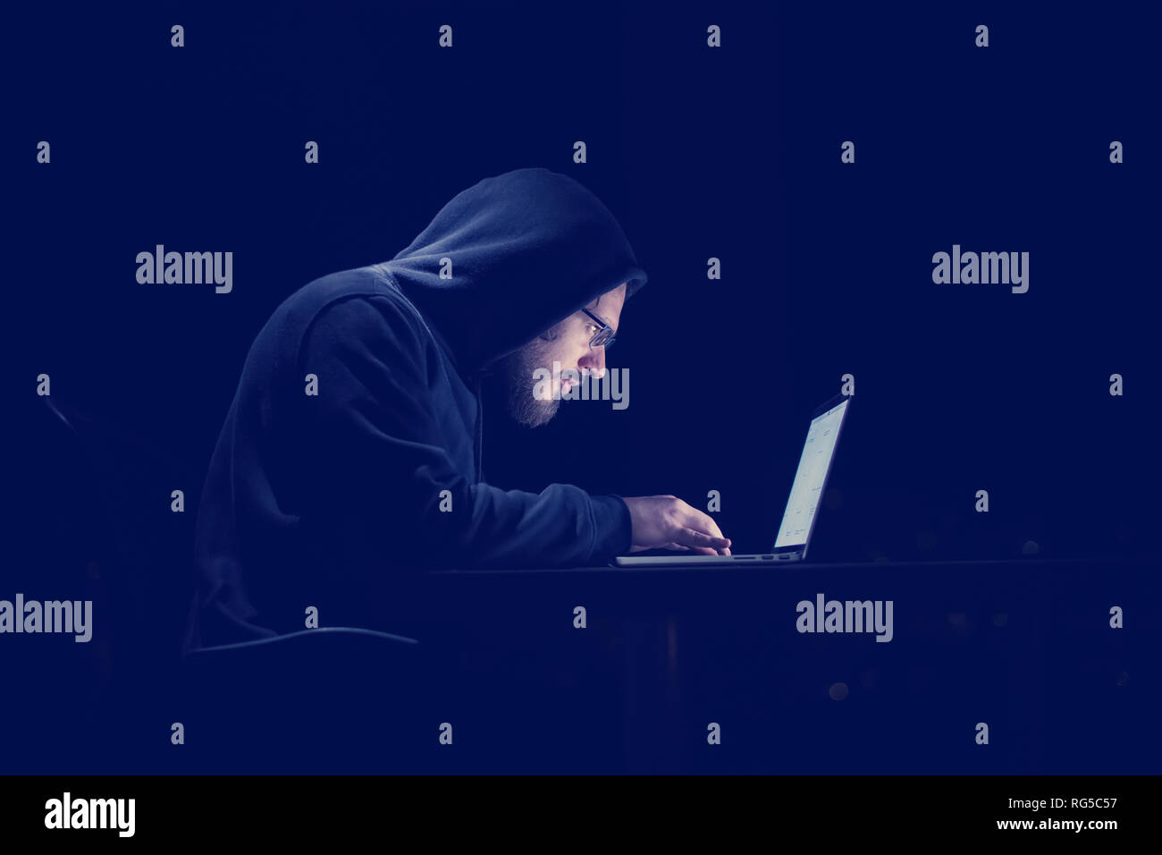 Young talented hacker using laptop computer while working in dark ...