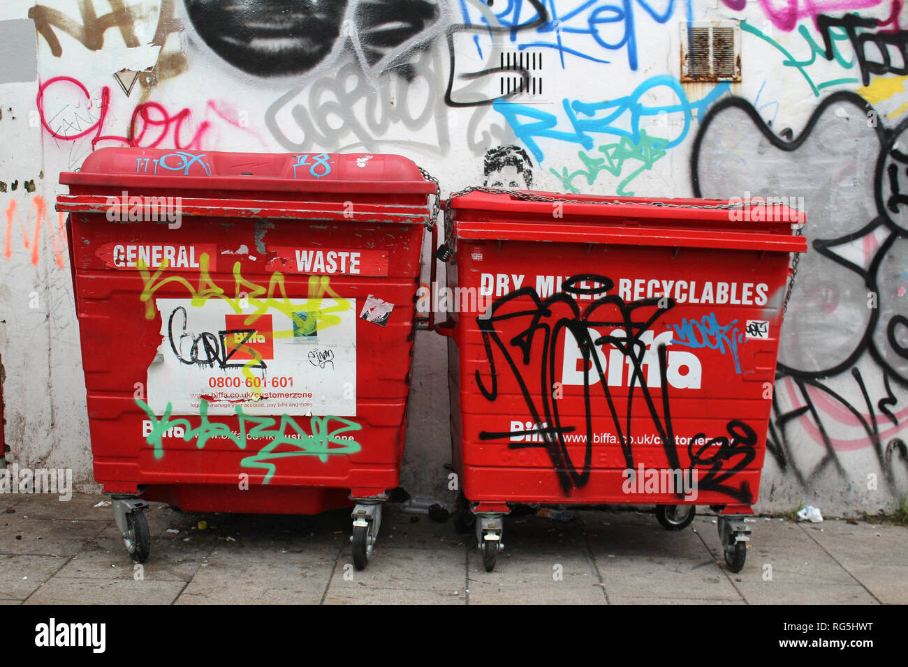 Two red general waste bin in front of a wall with graffiti , Brighton & Hove; England; UK Stock Photo