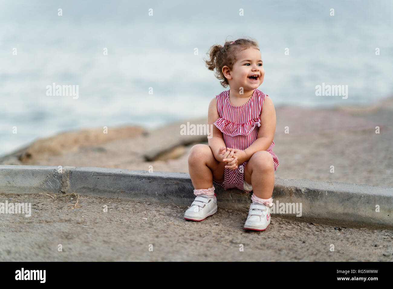 toddler girl sitting on concrete sidewalk.Natural light. Selective focus. Stock Photo