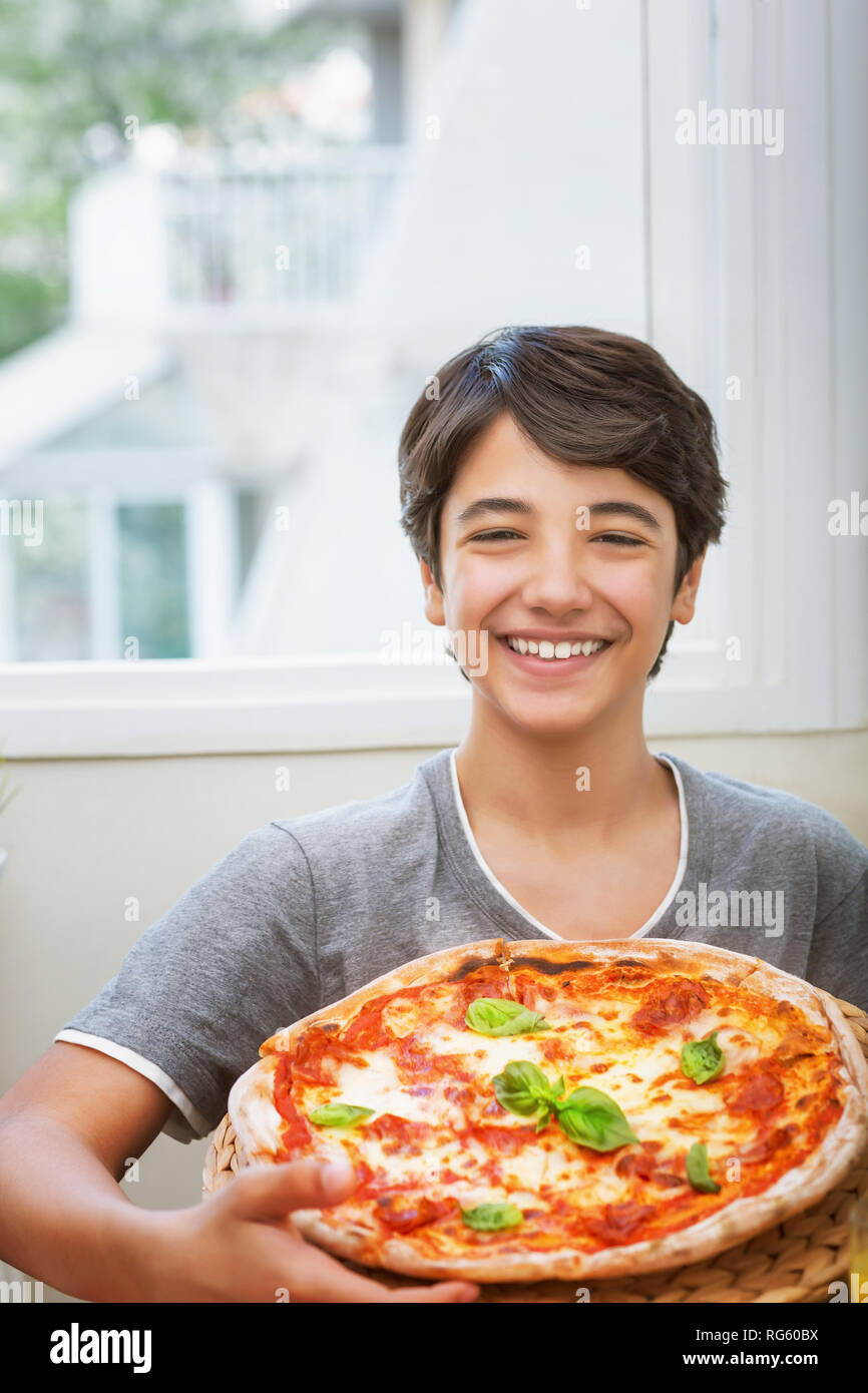 Happy teen boy cooked pizza, cheerful smiling teenager holding homemade pizza, enjoying traditional tasty italian food Stock Photo
