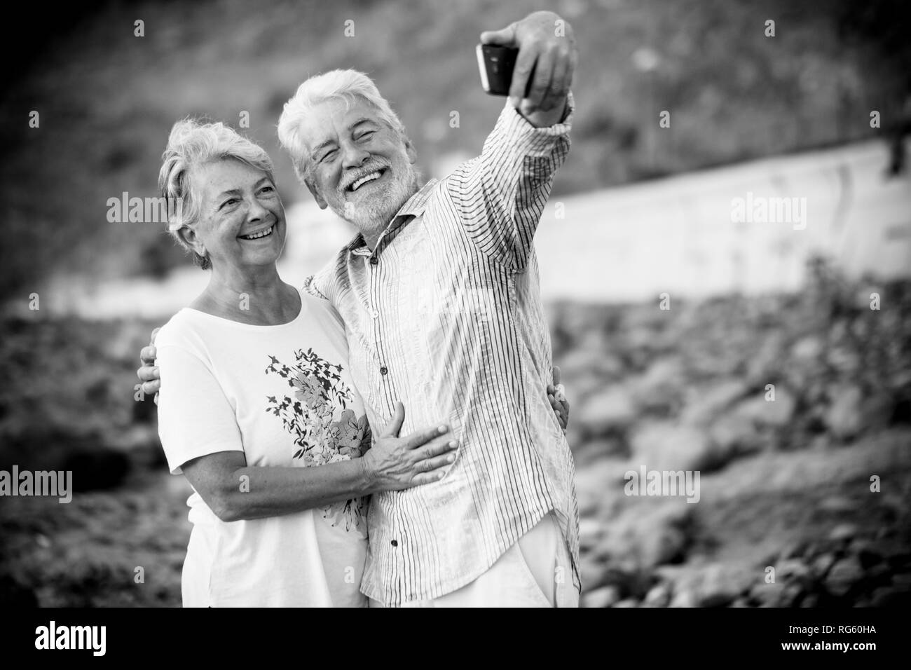 Black and white image retro concept filter - couple of happy smiling cheerful aged elderly people taking selfie picture with modern smart phone to sha Stock Photo