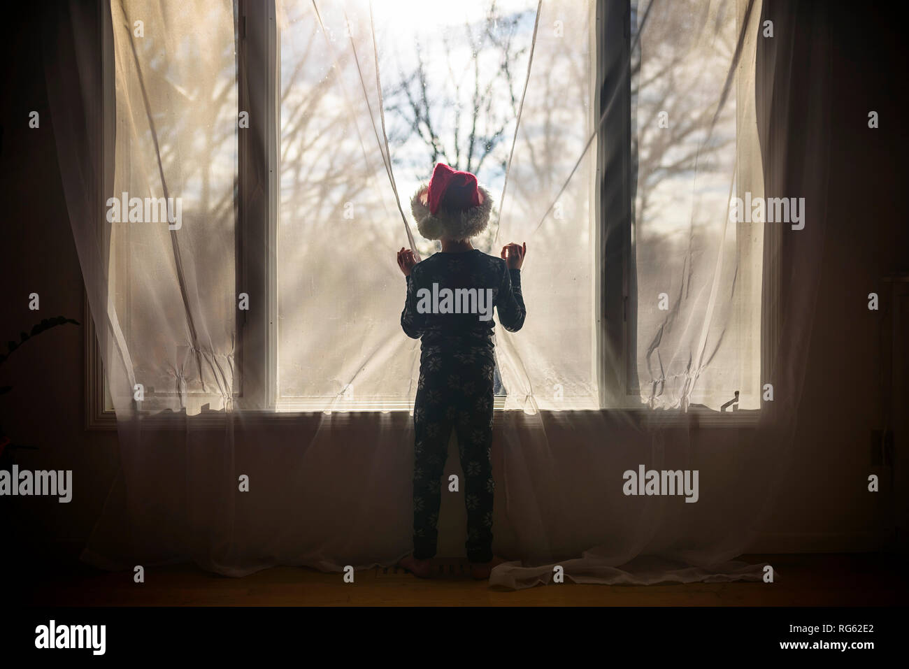 Boy wearing a Santa Hat looking through a window Stock Photo