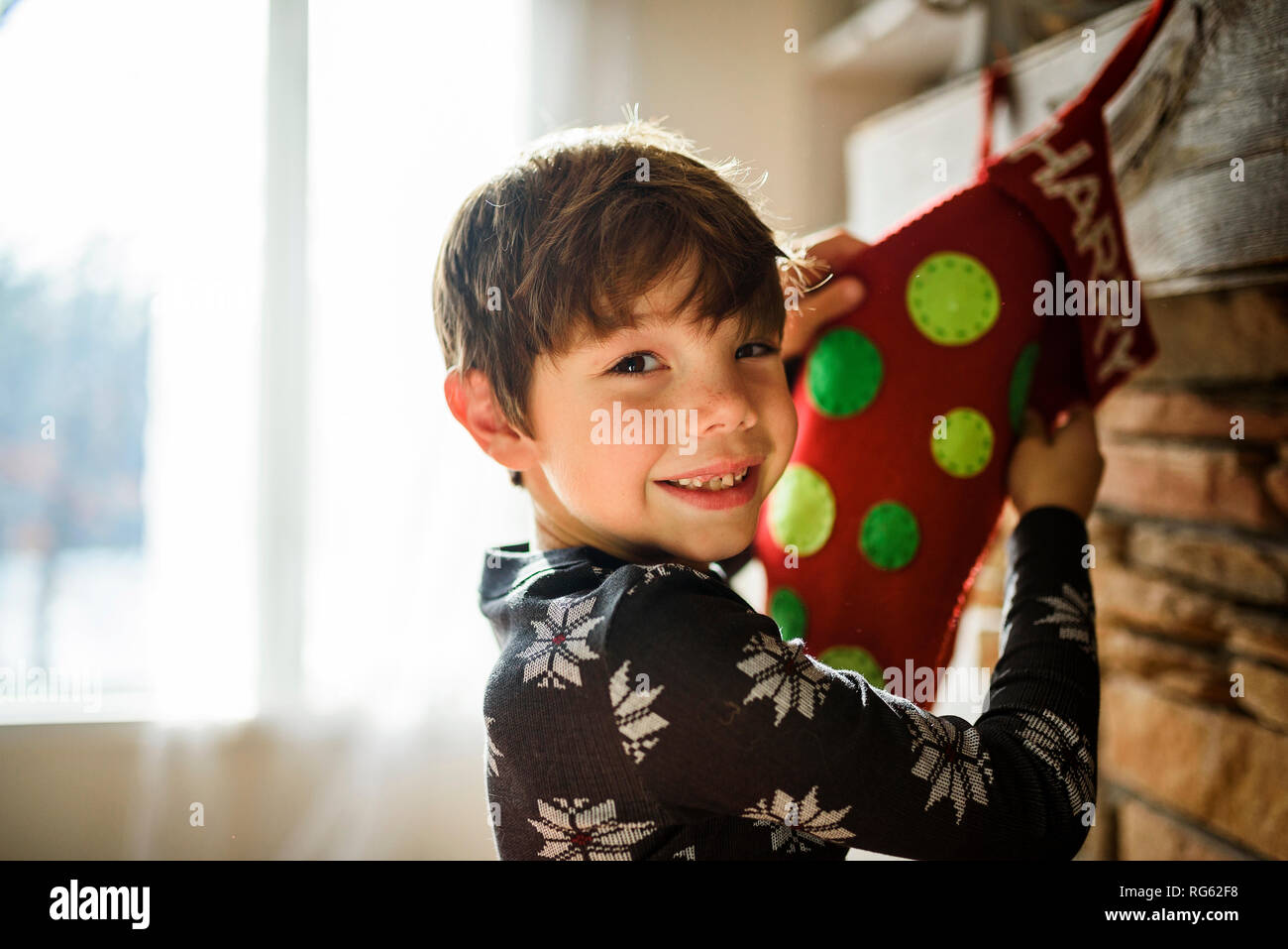 Smiling Boy hanging a Christmas stocking on a fireplace Stock Photo