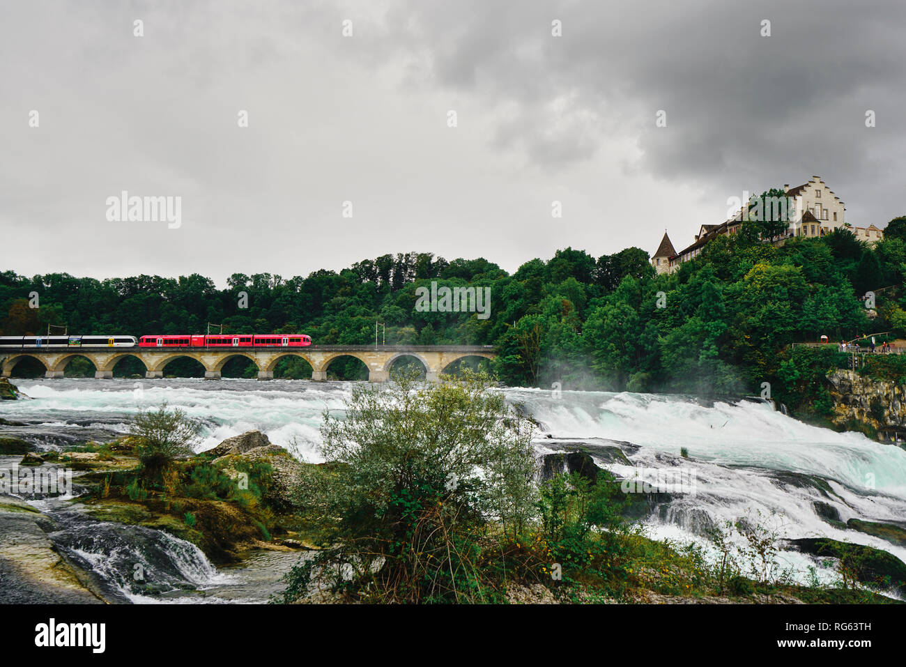 Red train on railway bridge at Rhine Falls (Rheinfall). Rhinefall is ...