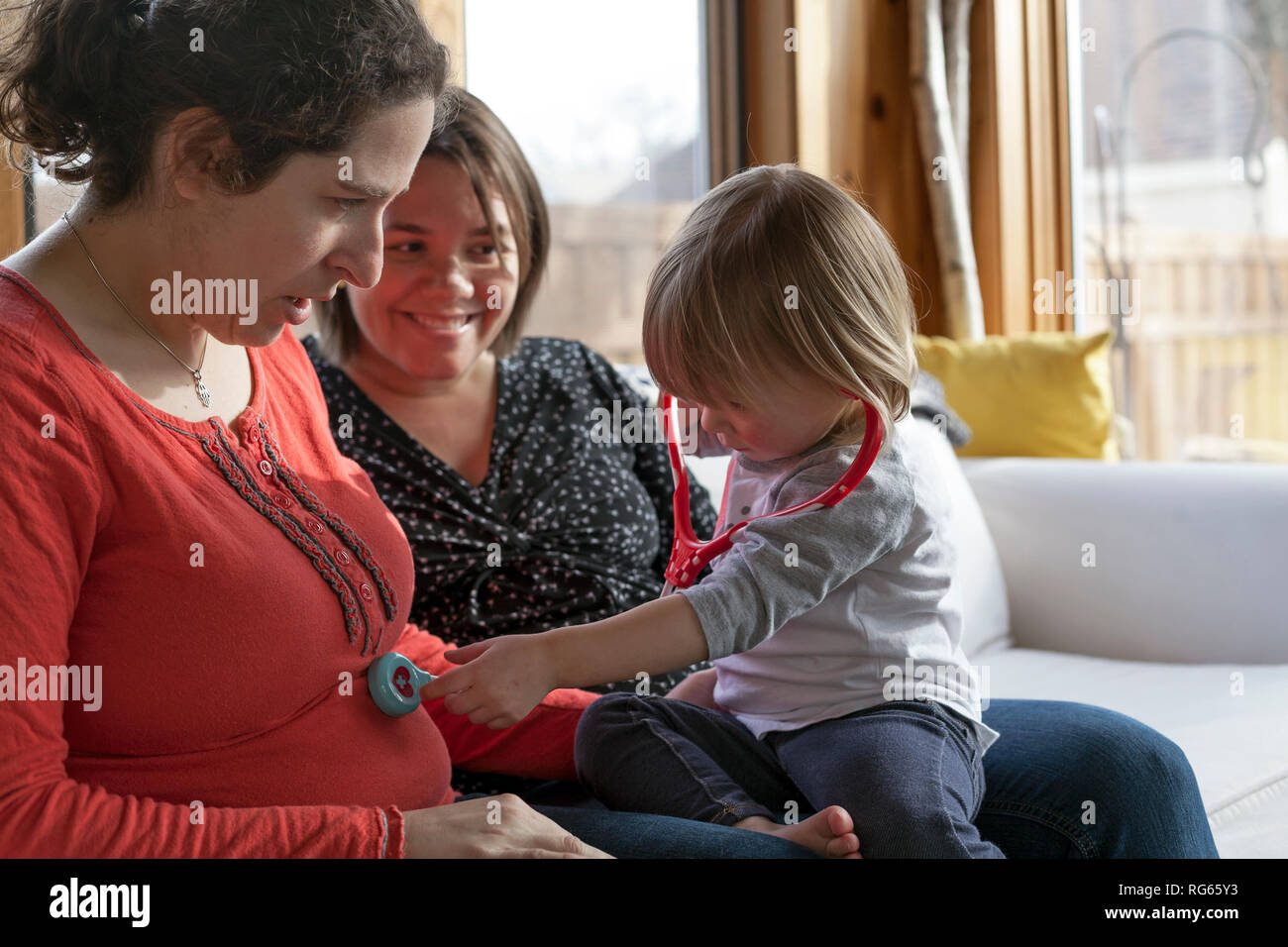 A toddler uses a stethoscope on a pregnant woman. Stock Photo