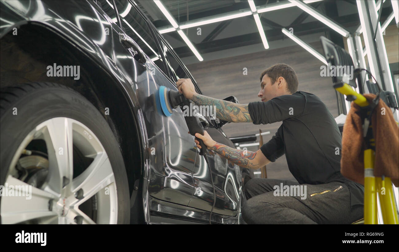 A man polishes a gray car body, a tool for polishing cars, into a workshop.  Deteyling auto. Polished black car body Stock Photo - Alamy