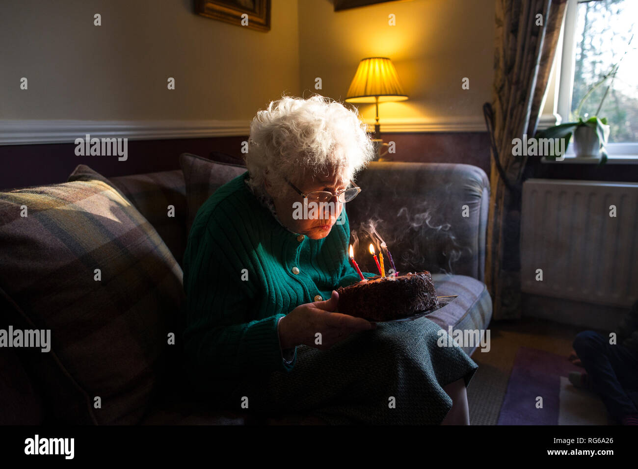 Elderly woman celebrating her birthday with a cake whilst blowing out the candles, England, United Kingdom Stock Photo