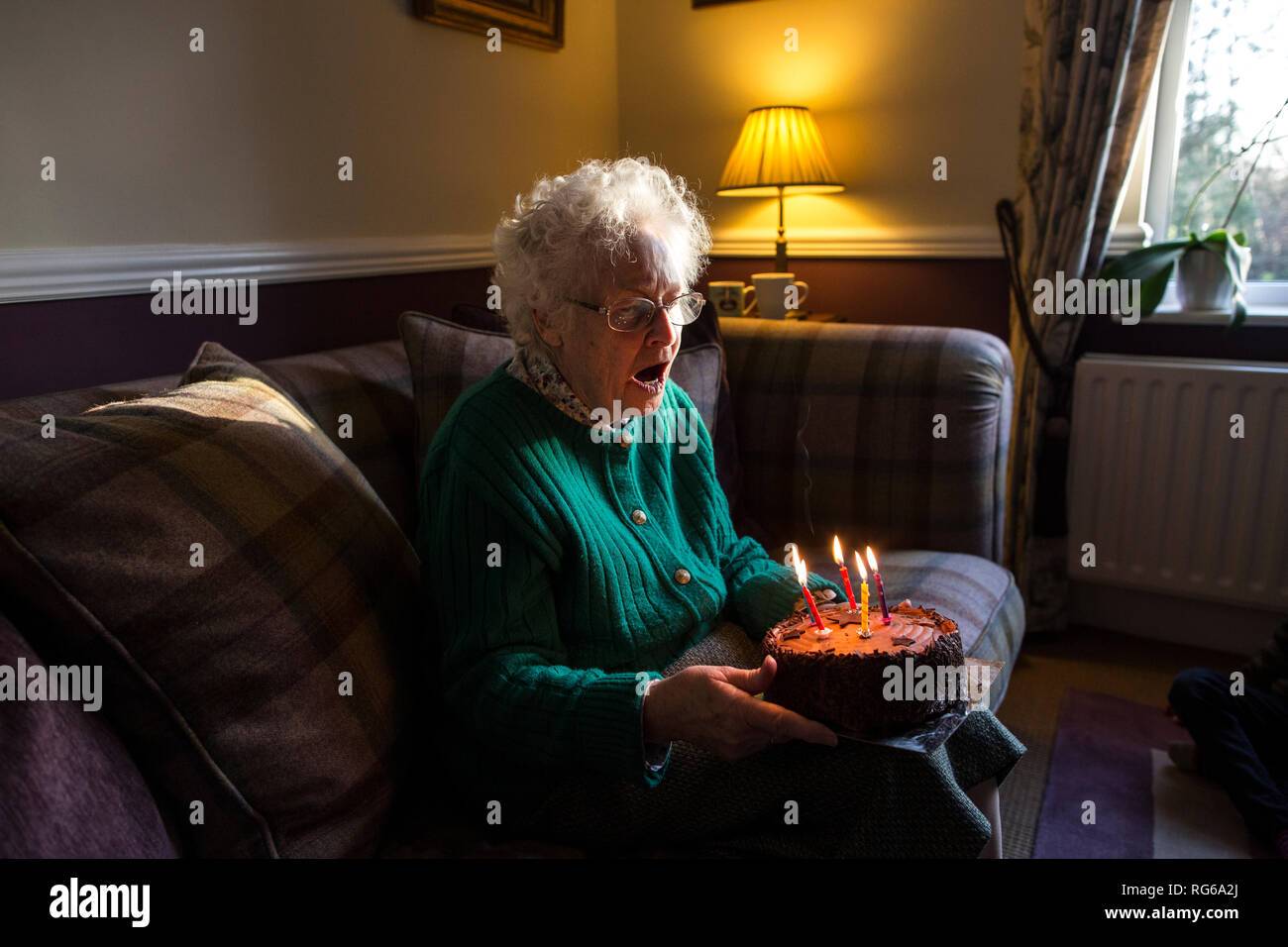 Elderly woman celebrating her birthday with a cake whilst blowing out the candles, England, United Kingdom Stock Photo