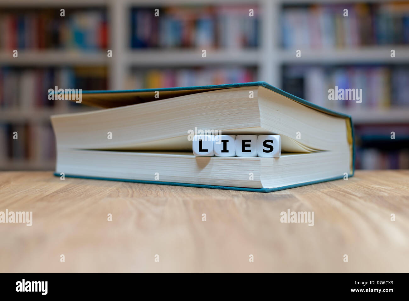 Dice in a book form the German word 'lies' ('read' in English). Book is lying on a wooden desk in front of a bookshelf. Stock Photo