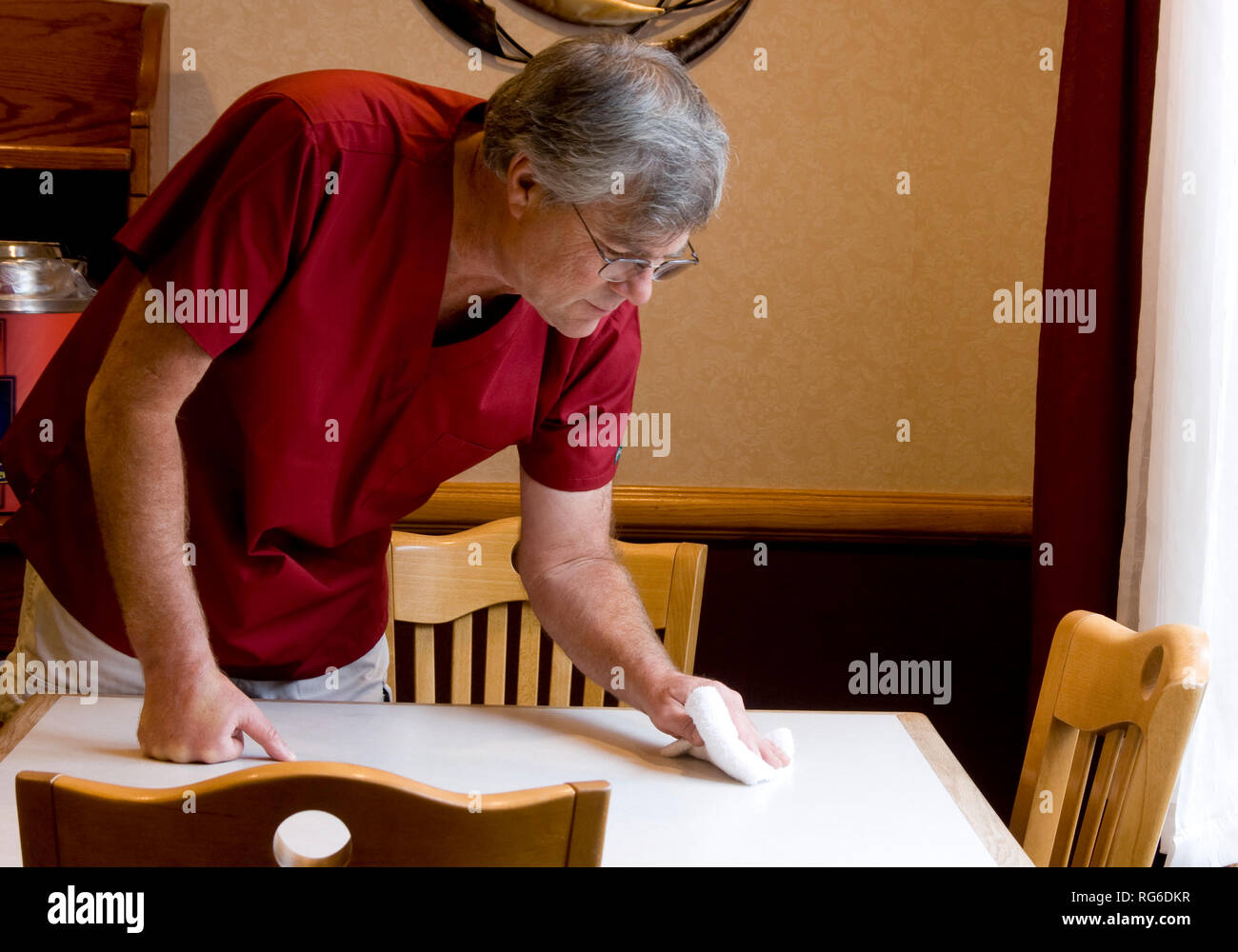 Worker cleaning a table in a restaurant setting Stock Photo