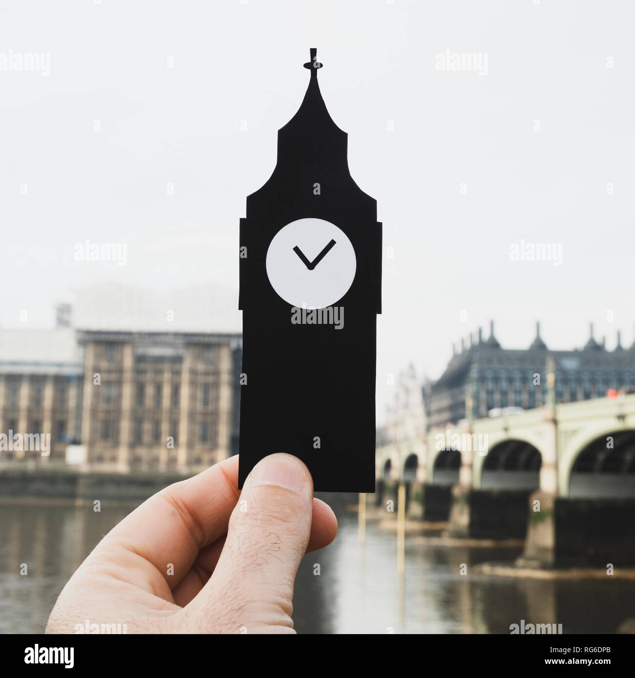 closeup of the hand of a man holding a paper cutout in the shape of the Clock Tower of the Palace of Westminster in London, United Kingdom Stock Photo