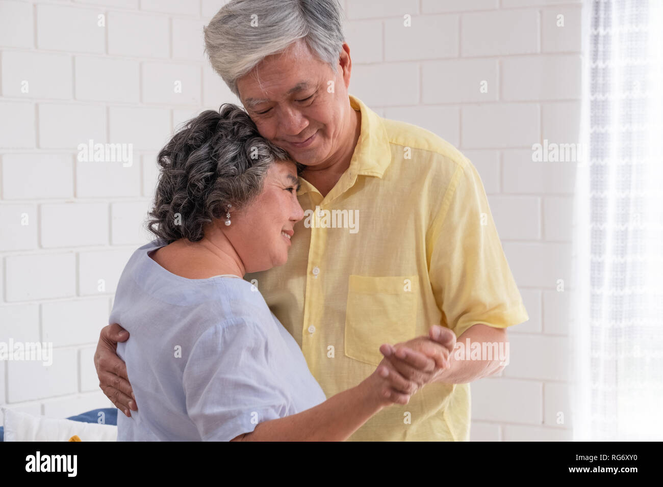 Happy Asian senior couple enjoy slow dancing at living room in house with warm love emotion.grandmother snuggle grandfather Stock Photo