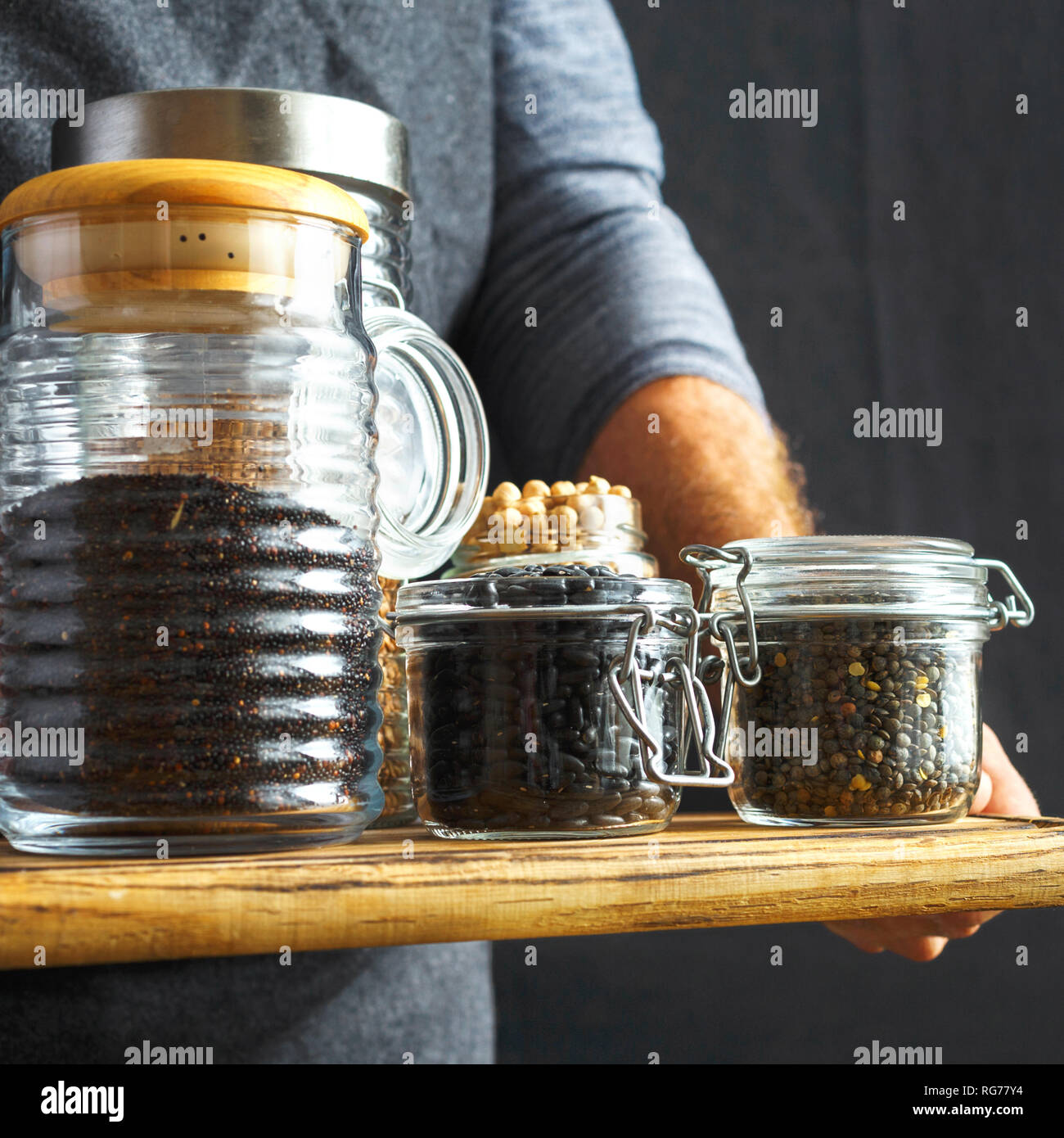 Set groats glass jars in hands man: black quinoa, chickpeas, black beans, green lentils, buckwheat dark background healthy vegan food concept Stock Photo