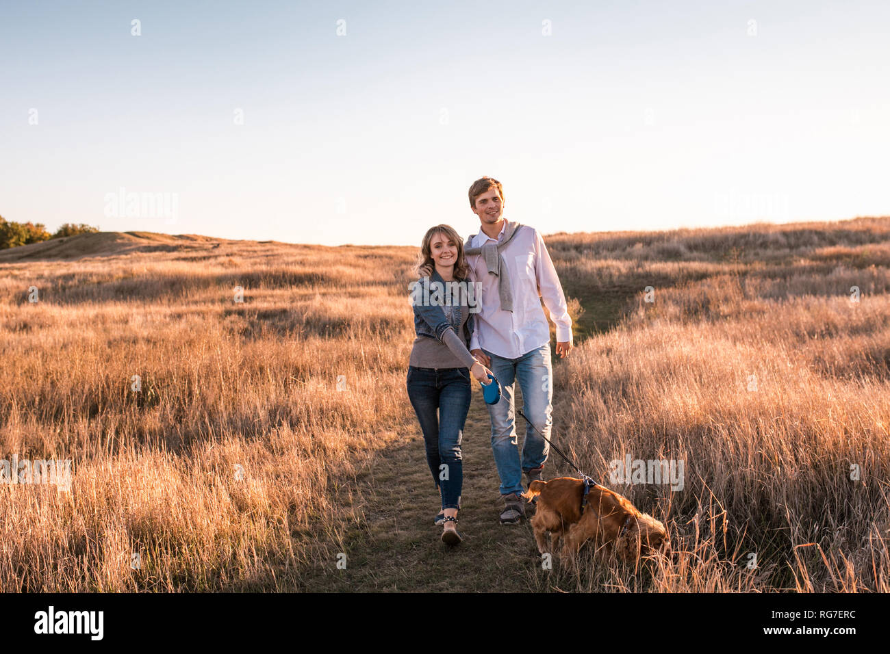 Happy young couple is walking with dog Stock Photo - Alamy