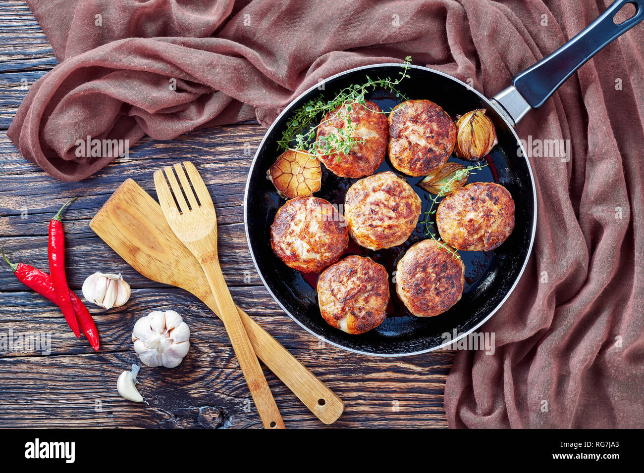 homemade fried meat cutlets, patties of chopped meat in a skillet with thyme, garlic and onion on an old wooden table with brown cloth, view from abov Stock Photo