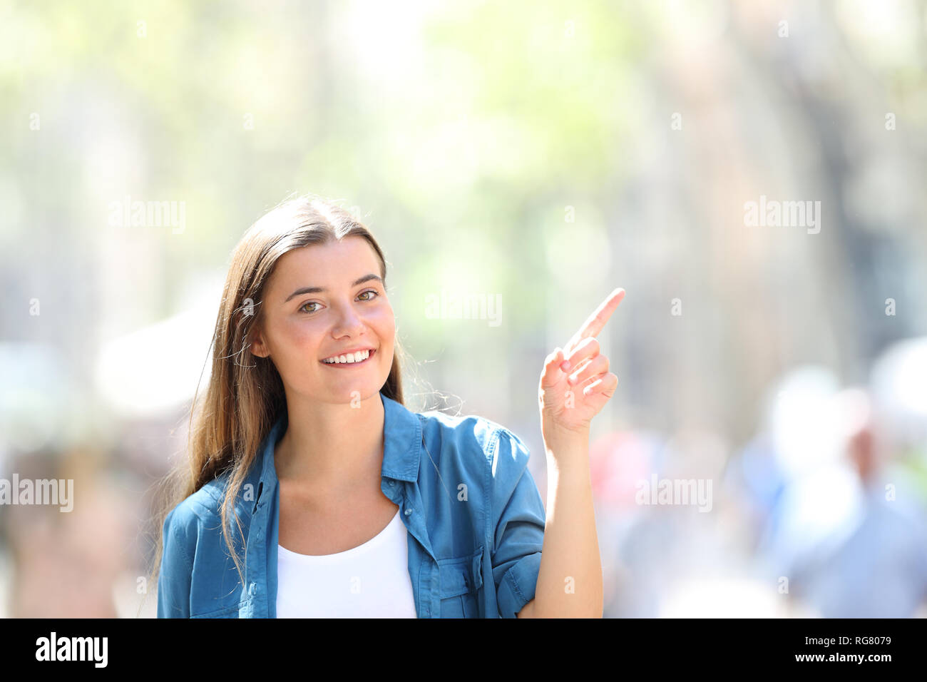 Front view portrait of a happy girl pointing at side in the street looking at you a sunny day Stock Photo