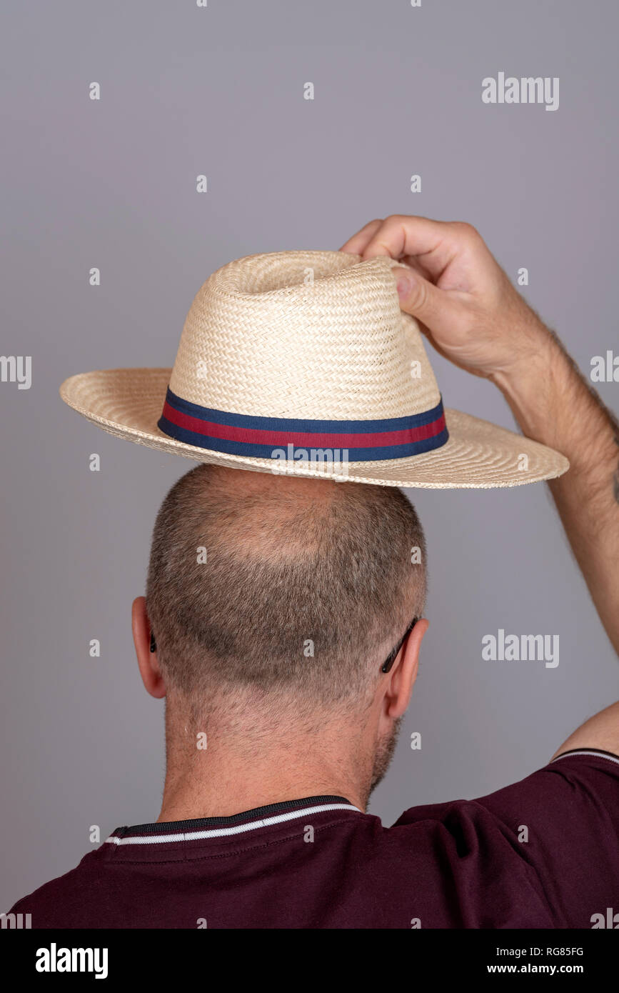 Balding man putting on a straw hat for sun protection. Stock Photo