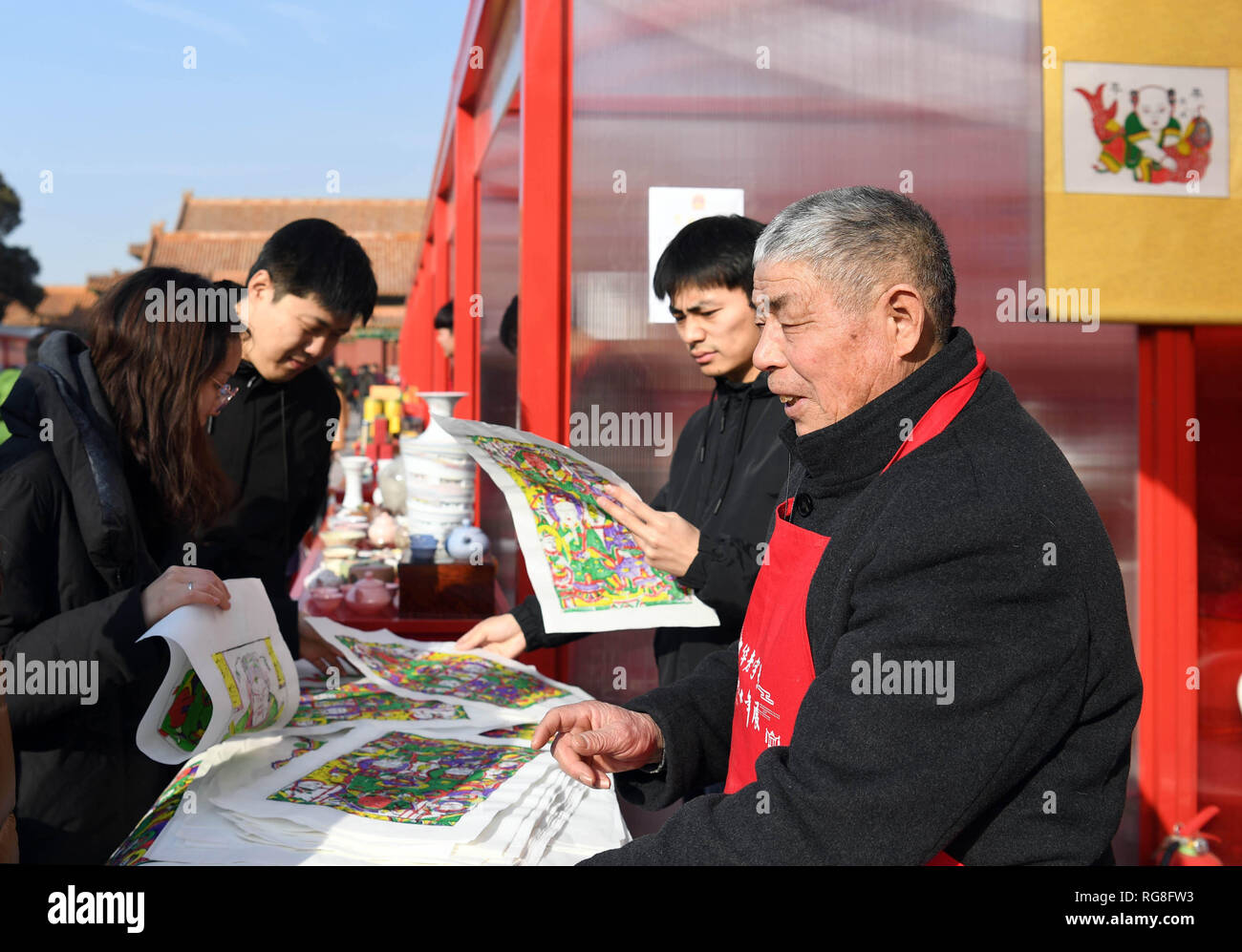 (190128) -- BEIJING, Jan. 28, 2019 (Xinhua) -- Folk artist Yin Guoquan (1st R) introduces New Year paintings to tourists during a fair at the Palace Museum in Beijing, capital of China, Jan. 28, 2019. About 150 Chinese time-honored brands, selected from some Chinese provinces and municipalities, are exhibited at a fair in the Palace Museum during the Spring Festival. The histories of many of the Chinese time-honored brands, ranging from local delicacies, liquors, health products to silk and handicrafts, can be traced back to the Qing Dynasty (1644-1911) when their products were exclusive tribu Stock Photo