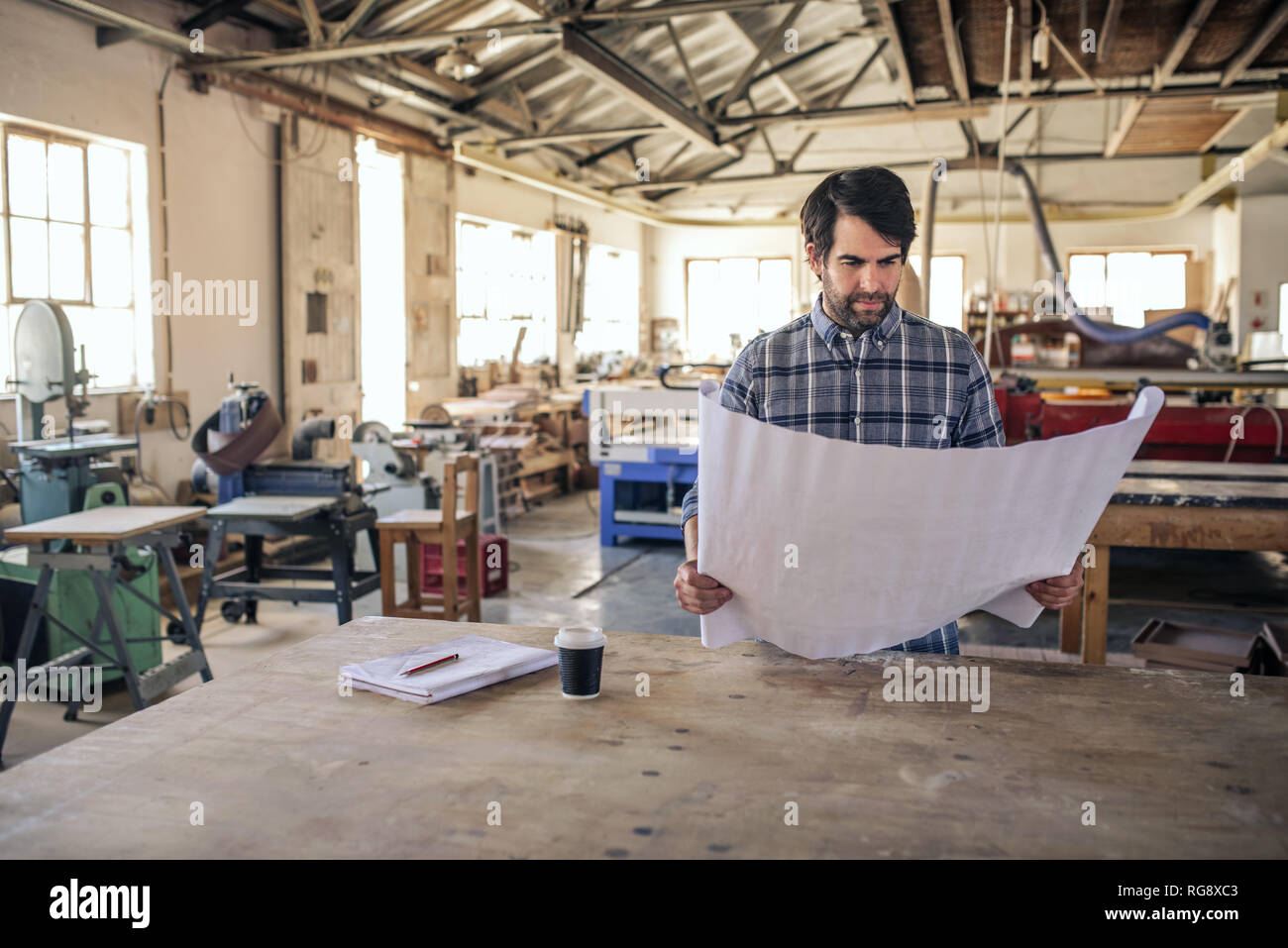 Woodworker reading design blueprints by a table Stock Photo