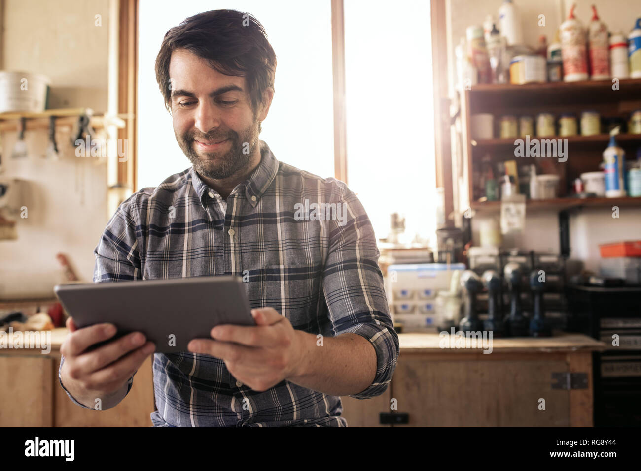 Smiling woodworker using a digital tablet in his workshop Stock Photo