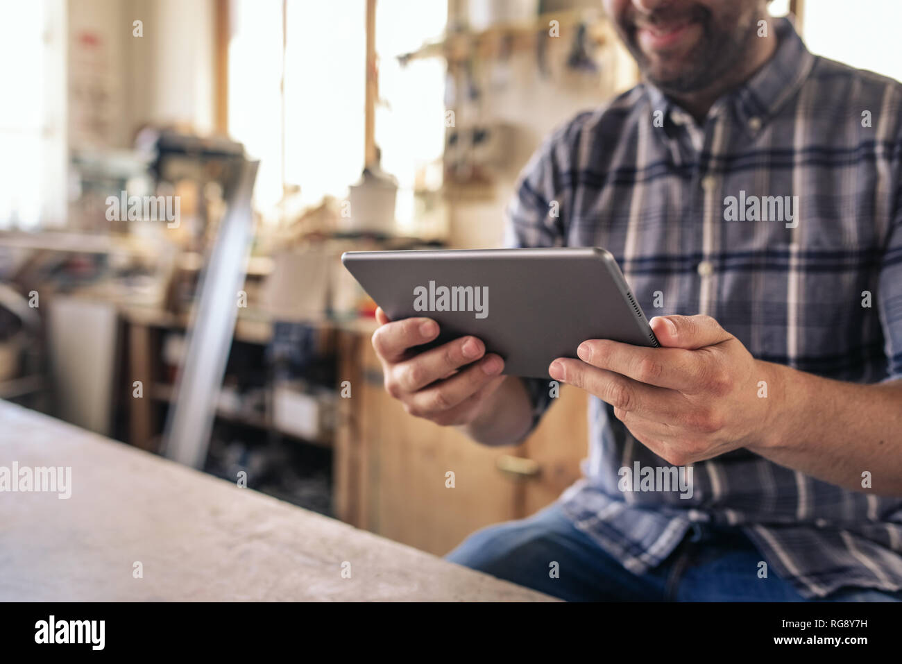 Woodworker sitting in his workshop using a digital tablet Stock Photo