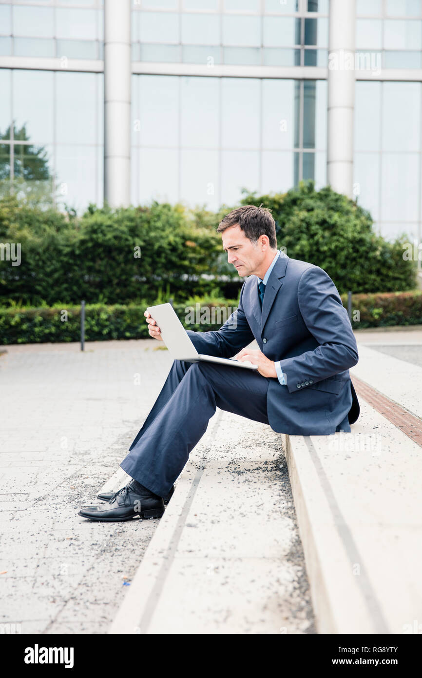 Serious businessman sitting down using laptop in the city Stock Photo