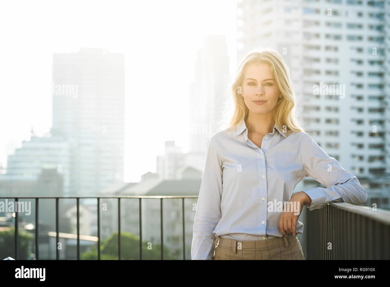 Portrait of blonde business woman leaning onto handrail on city rooftop Stock Photo