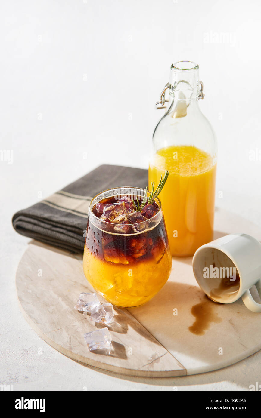 Ice cold summer drink. Orange juice espresso with ice, bottle of organic orange juice and empty espresso shot on white marble serving plate over white Stock Photo