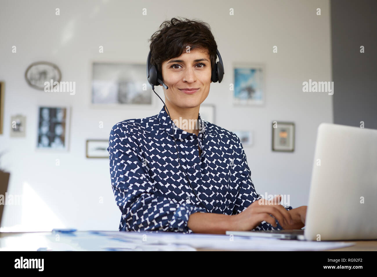 Portrait of smiling woman at home with headset and laptop Stock Photo