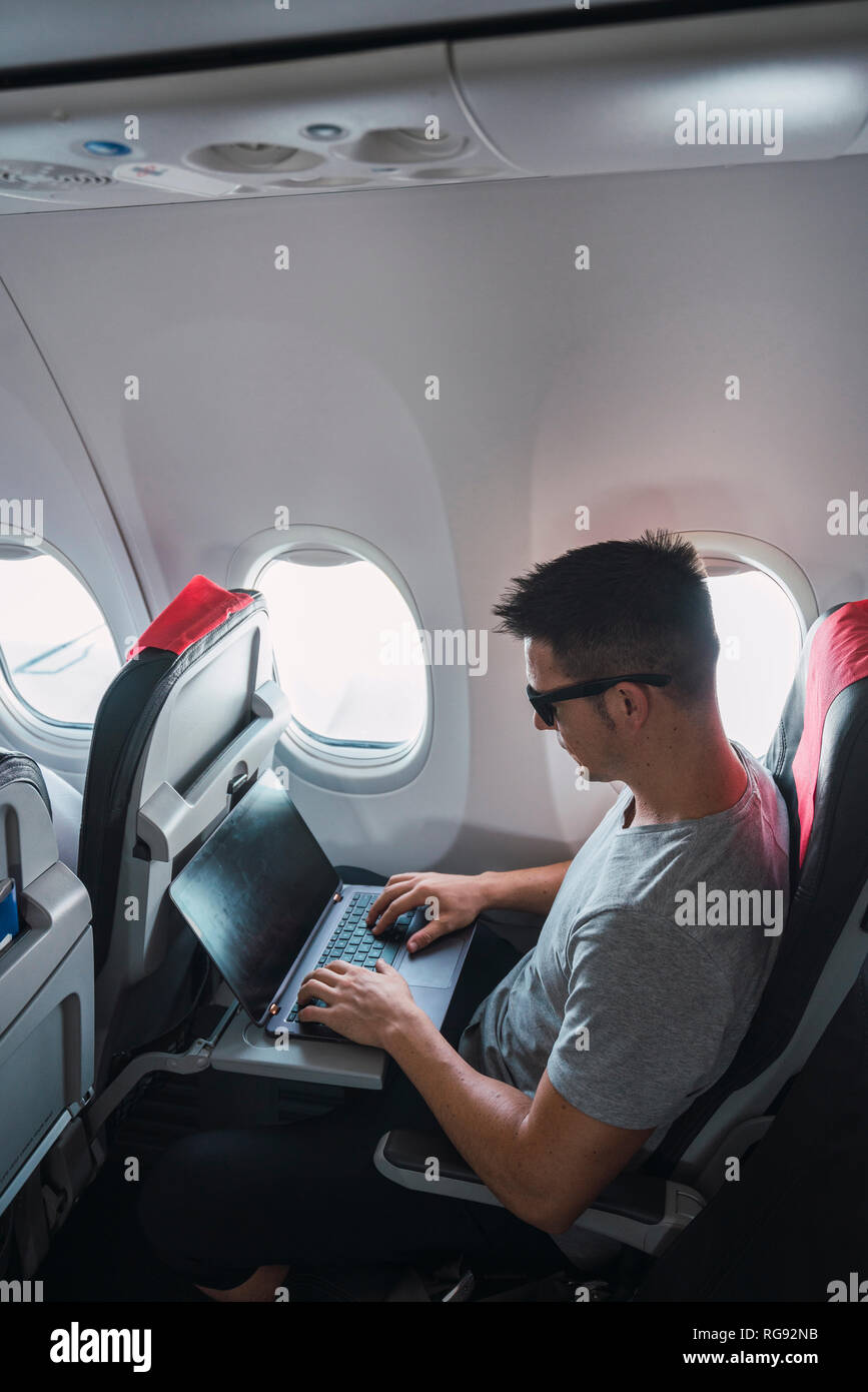 Man using laptop in airplane Stock Photo
