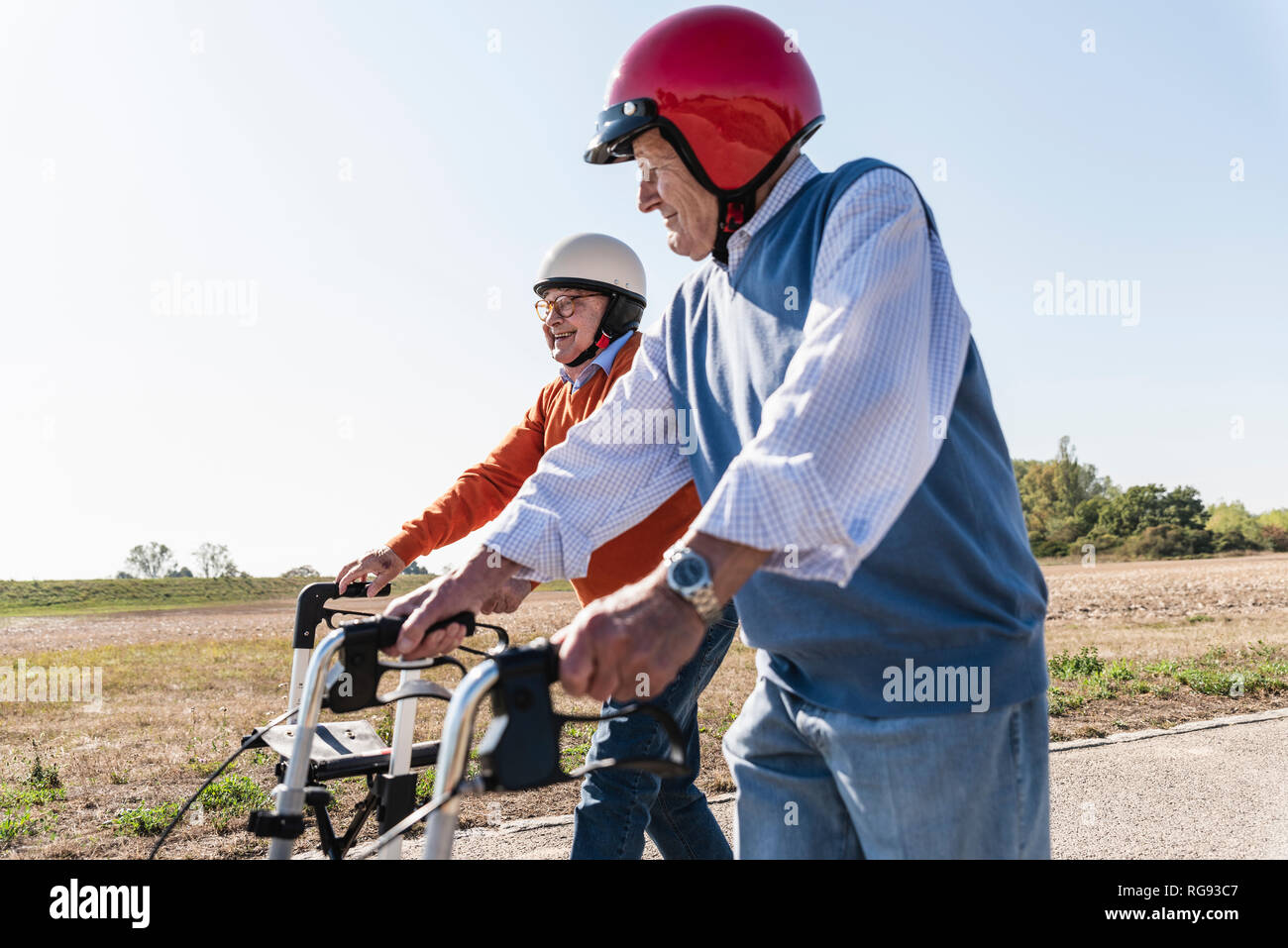 Two old friends wearing safety helmets, competing in a wheeled walker race Stock Photo