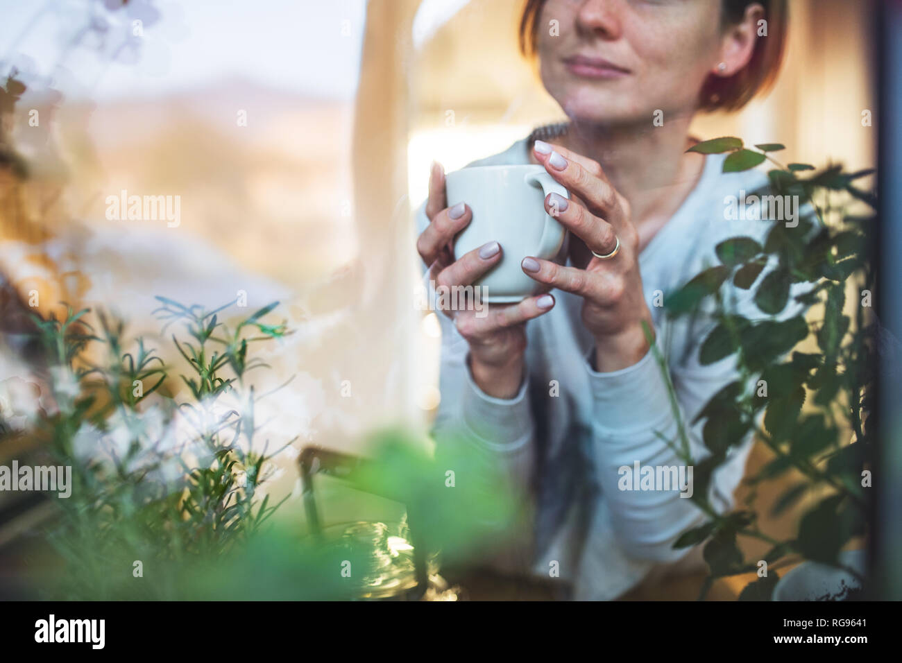 A midsection of young woman with cup of coffee looking out of a window. Shot through glass. A copy space. Stock Photo