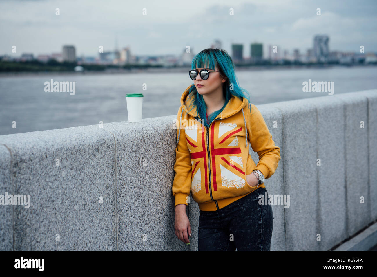 Portrait of young woman with dyed blue hair wearing fashionable hooded jacket looking at distance Stock Photo