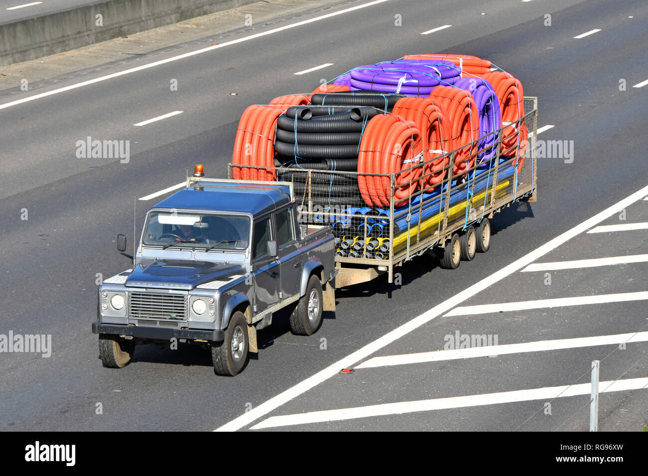 View looking down on Land Rover Defender & trailer transport of assorted colour coil & straight flexible plastic pipe tubing driving along UK motorway Stock Photo