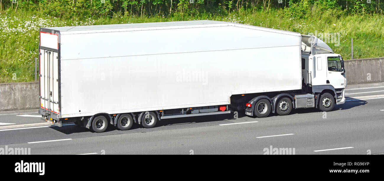 Side & back view of aerodynamic shape of long plain white unmarked clean hgv delivery lorry truck & articulated trailer driving along UK motorway road Stock Photo