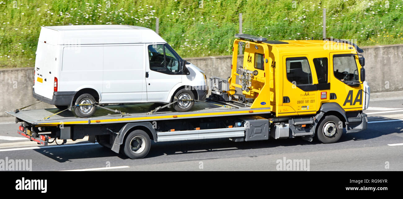 Looking down from above side view AA Renault breakdown truck transporting white Ford Transit van secured by webbing restraints driving on UK motorway Stock Photo
