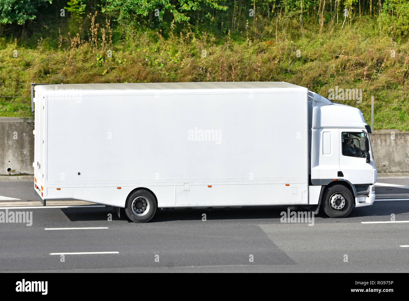 Side view of a clean unmarked all white hgv  lorry truck van transport with cab & driver without any advertising driving along M25 motorway England UK Stock Photo