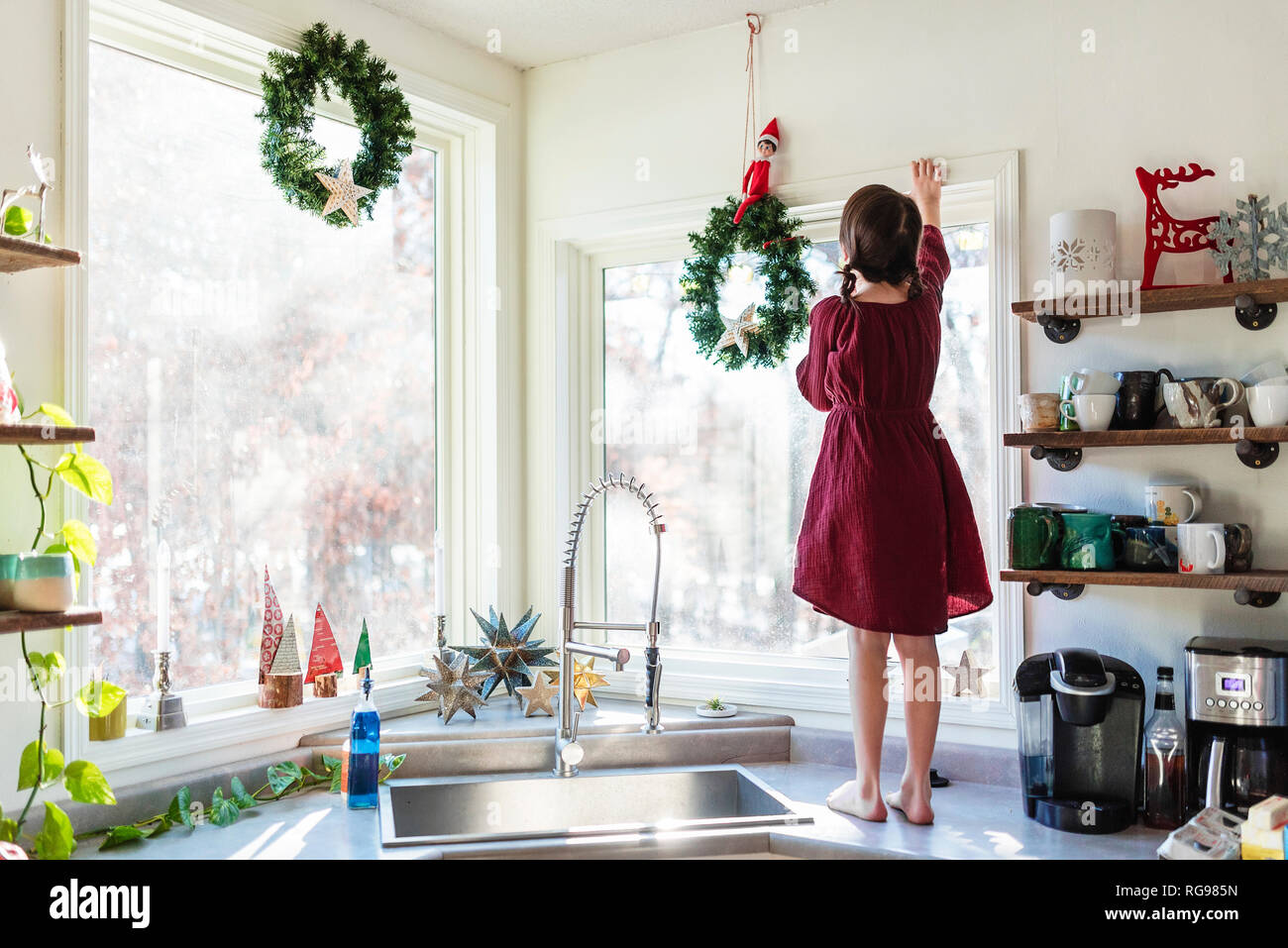 Girl standing on a kitchen worktop putting up  Christmas decorations Stock Photo