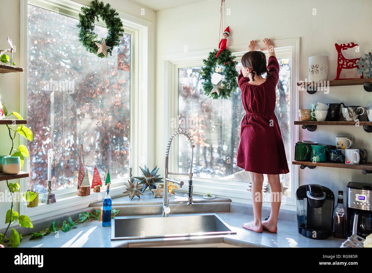 Girl standing on a kitchen worktop putting up Christmas decorations Stock Photo