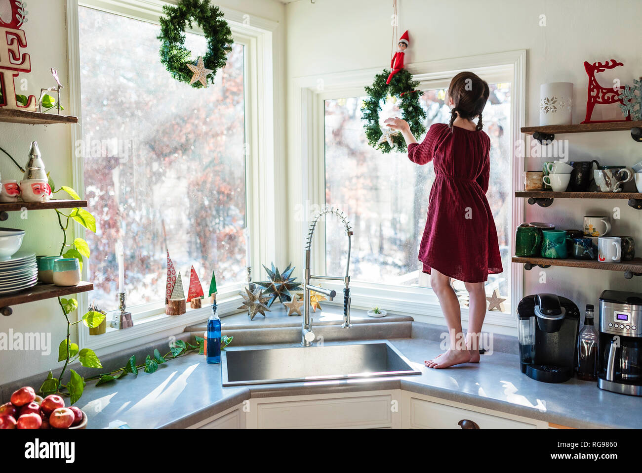 Girl standing on a kitchen worktop putting up Christmas decorations Stock Photo