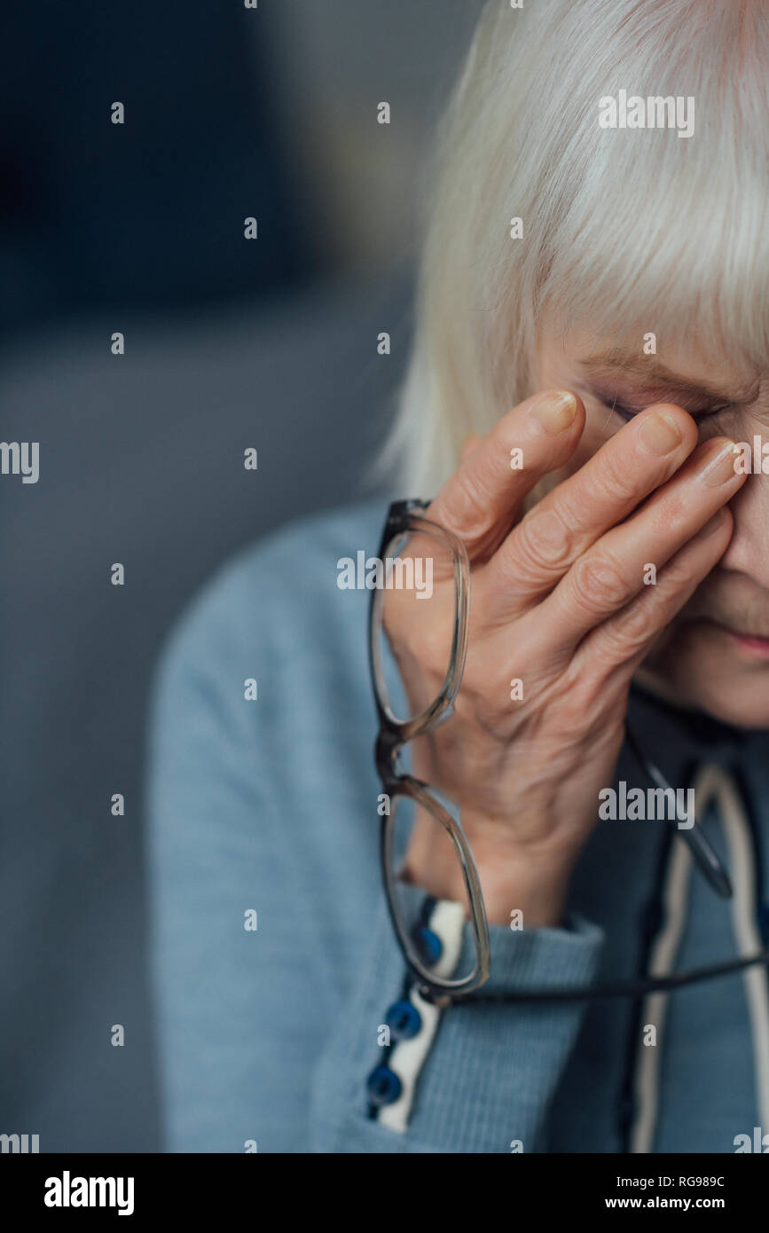 senior woman with glasses and grey hair wiping tears and crying at home Stock Photo