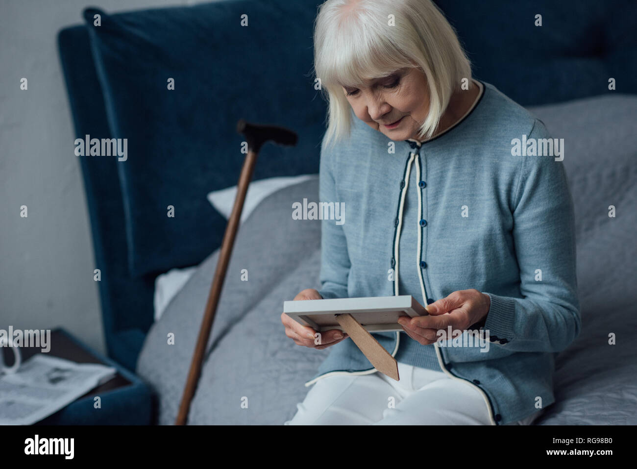senior woman sitting on bed and looking at photo frame at home Stock ...