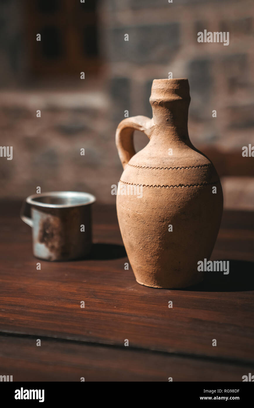 An old clay jug and with a glass stand on the wooden table. Stock Photo