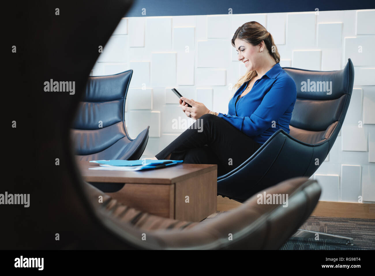 Happy Business Woman With Smartphone Sitting In Office Waiting Room Stock Photo