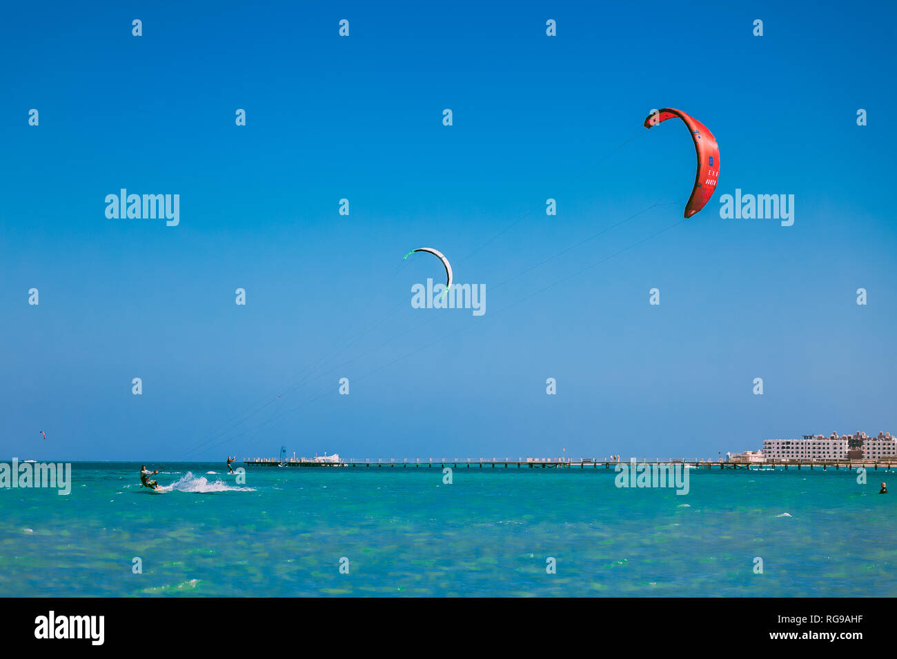 Egypt, Hurghada - 30 November, 2017: The red and white kites in the blue sky over the Red sea surface. The professional kitesurfers gliding on the wav Stock Photo