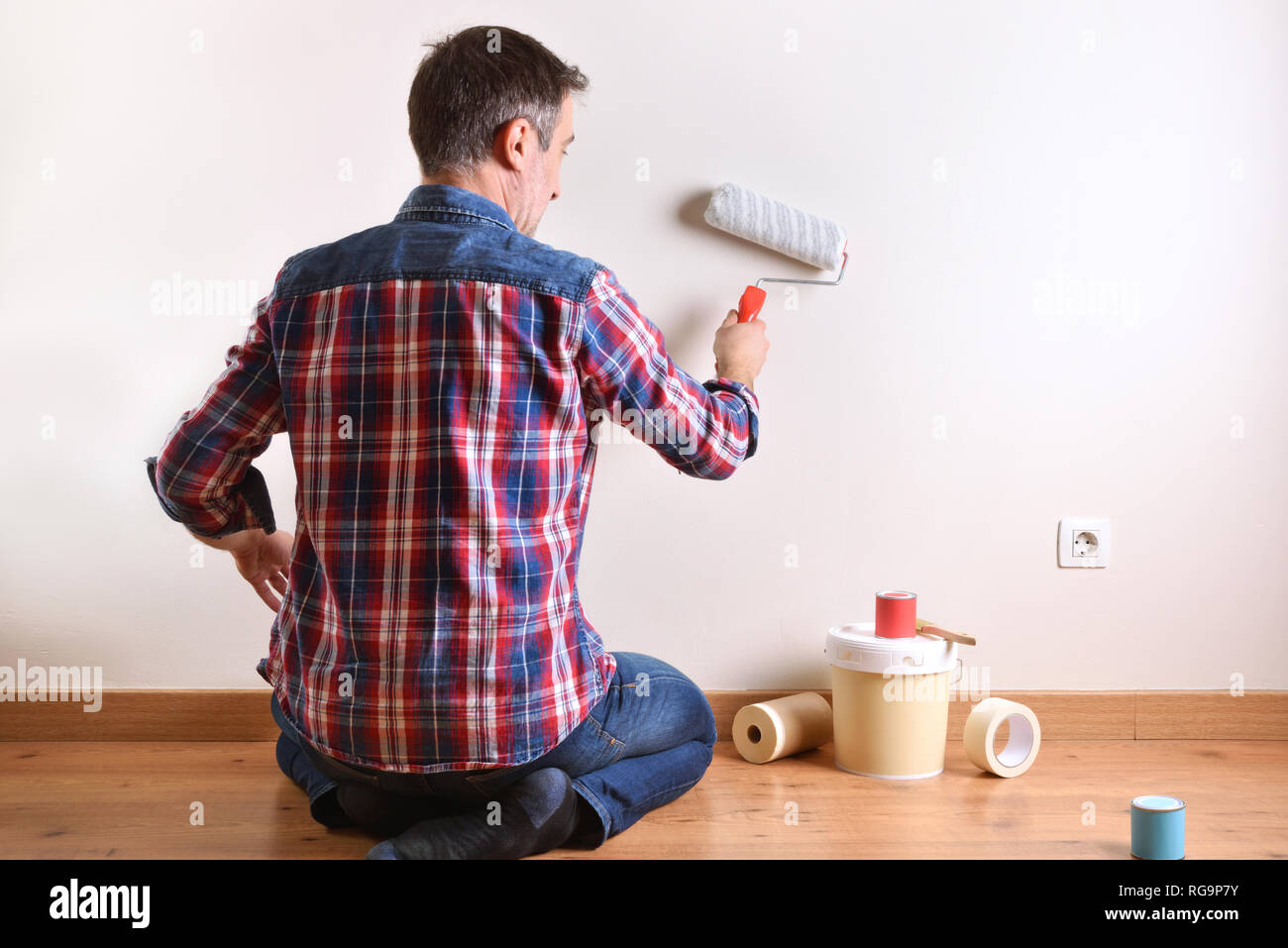 Man kneeling on a parquet floor with paint material painting his house. Front view. Horizontal composition. Stock Photo