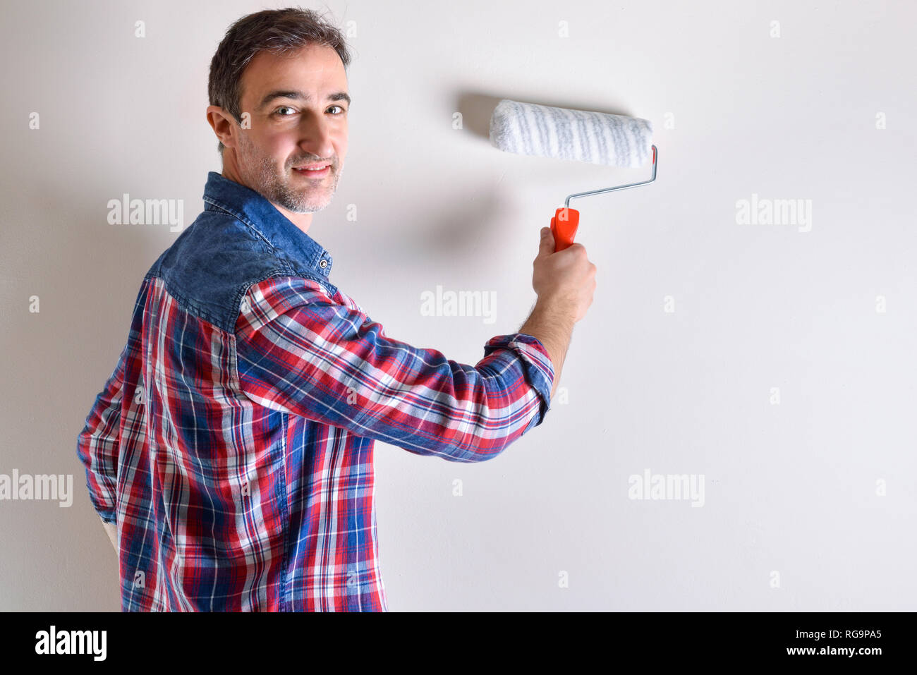 Man painting a white wall in his house. Diy home concept. Front view. Horizontal composition. Stock Photo