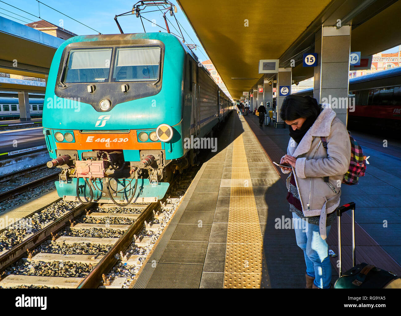Turin, Italy - December 30, 2018. A tourist consulting his mobile phone in front of a train of Trenitalia in an Italian train station. Turin, Piedmont Stock Photo